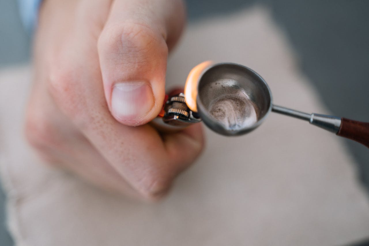 Detailed view of a hand using a lighter to heat a substance in a metal spoon.