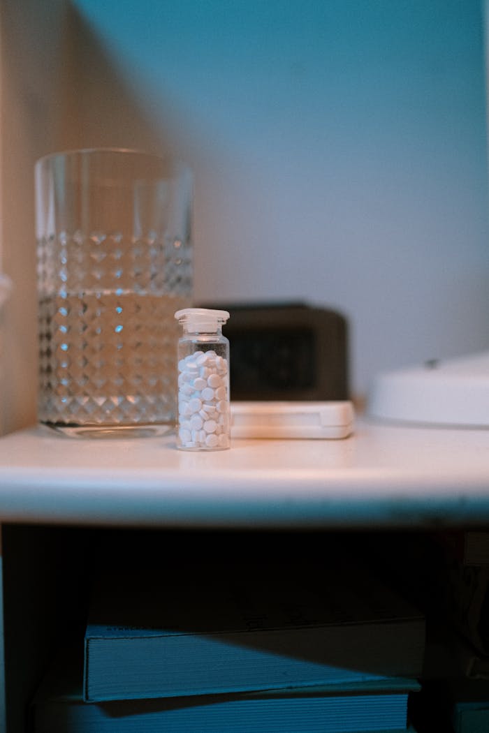 Close-up of a nightstand with a glass of water and a bottle of pills, suggesting evening routine.